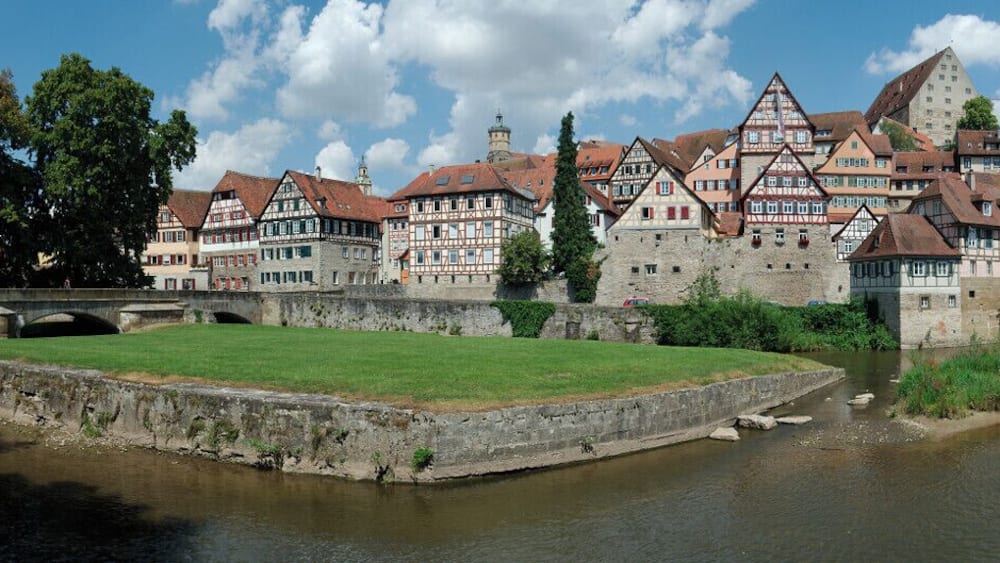 Eine historische Stadt mit einem Fluss, einer Steinbrücke und traditionellen Fachwerkhäusern.