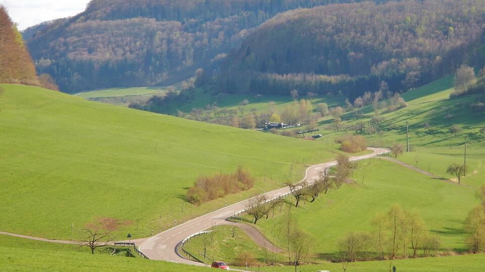 A winding road through a green valley with hills in the background.