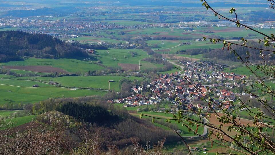 A panoramic view of a town nestled in a valley with surrounding green fields and distant hills.