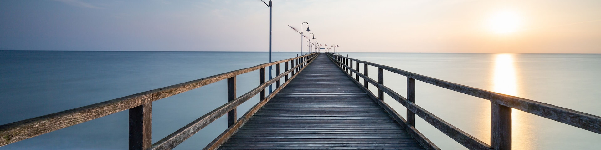 A wooden pier extending into calm waters at sunset.