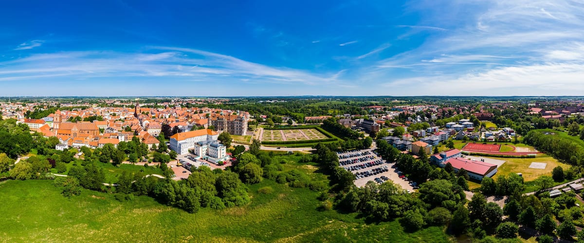A panoramic view of a town with a river, green parks, and historic buildings.