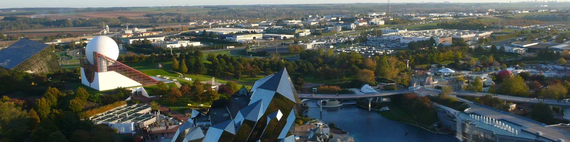 A modern architectural structure with a unique geometric design, a river, and a cityscape in the background.