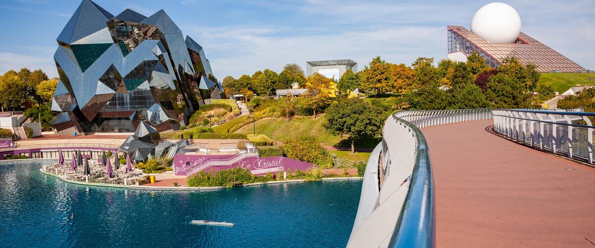 A modern architectural complex with a large spherical structure, a reflective water body, and a bridge.