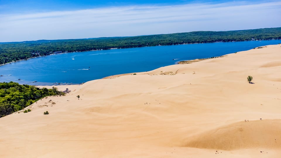 A coastal landscape with sand dunes, a clear blue lake, and a forested area.