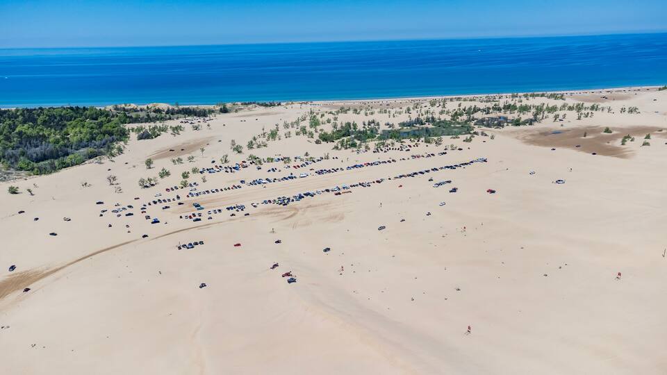 An aerial view of a desert landscape with a large number of parked vehicles and sparse vegetation.