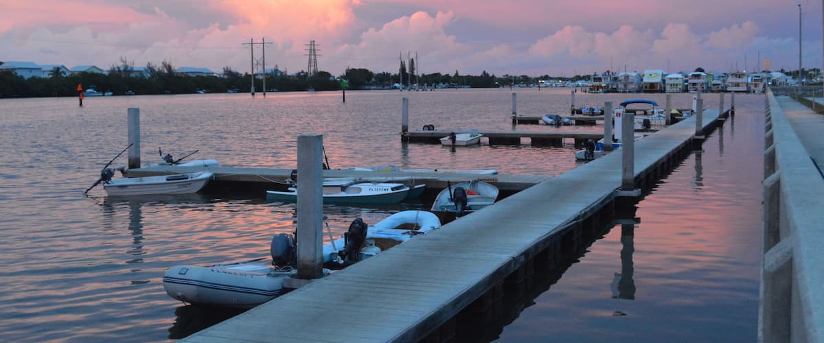 A marina with boats docked at wooden piers, a calm water body, and a sunset sky.