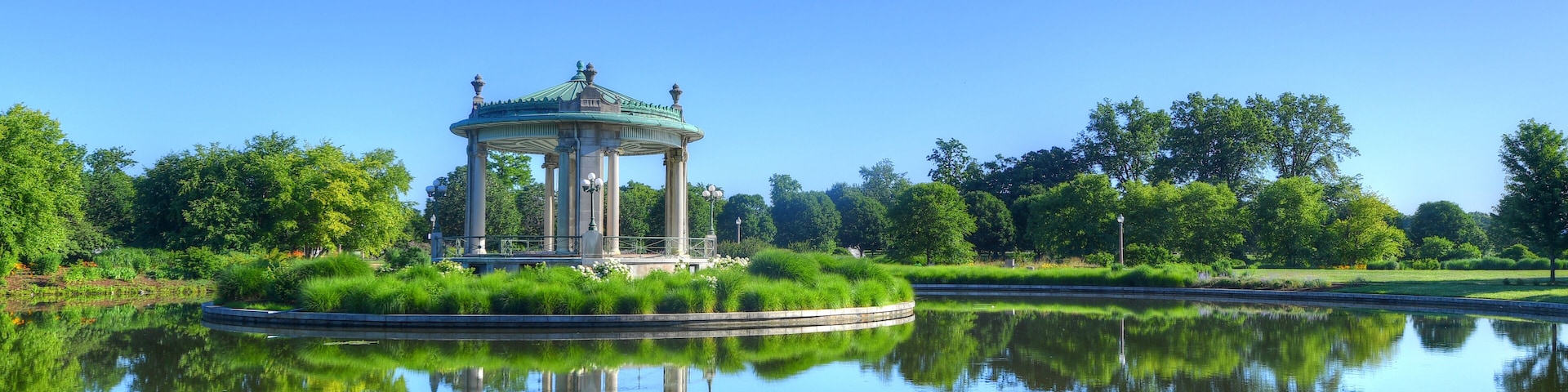 A gazebo by a calm lake with reflections of trees and sky.