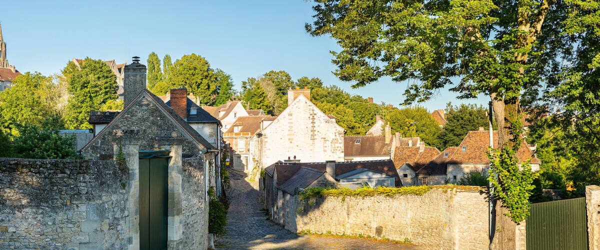 A narrow cobblestone street flanked by stone buildings and trees.