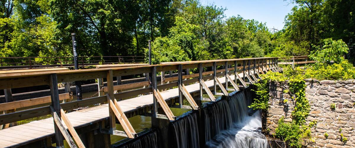 A wooden bridge over a waterfall with a stone wall on one side.