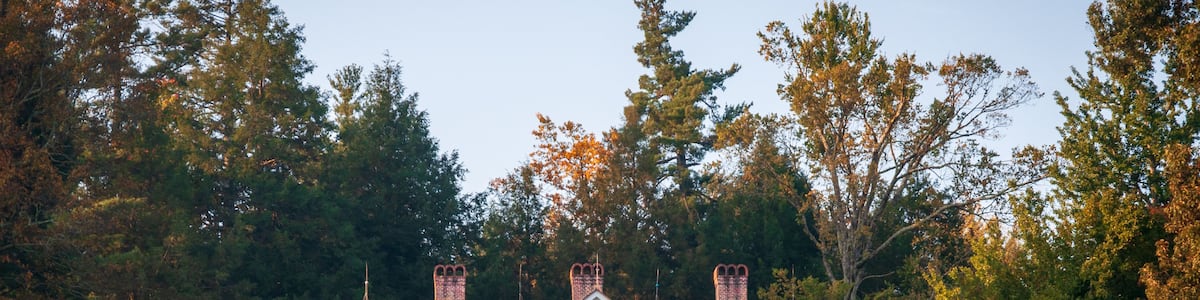 A white house with a porch, surrounded by a grassy field and trees.