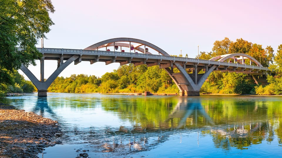 A bridge over a river with trees and a clear sky.
