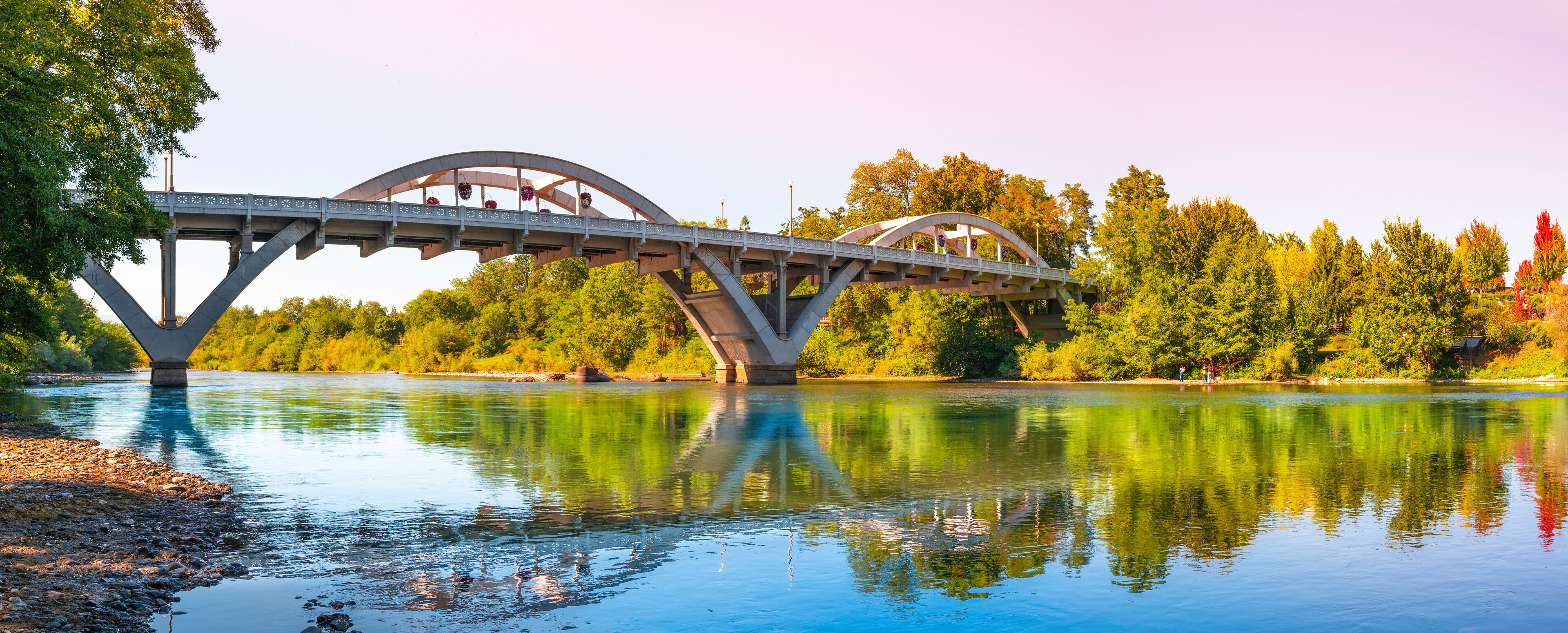 A bridge over a river with trees and a clear sky.