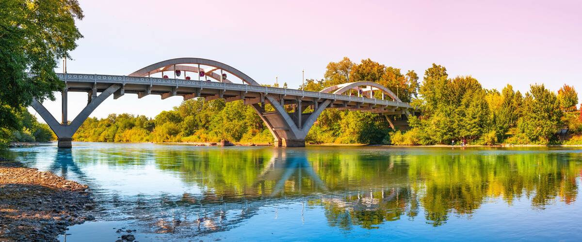 A bridge over a river with trees and a clear sky.