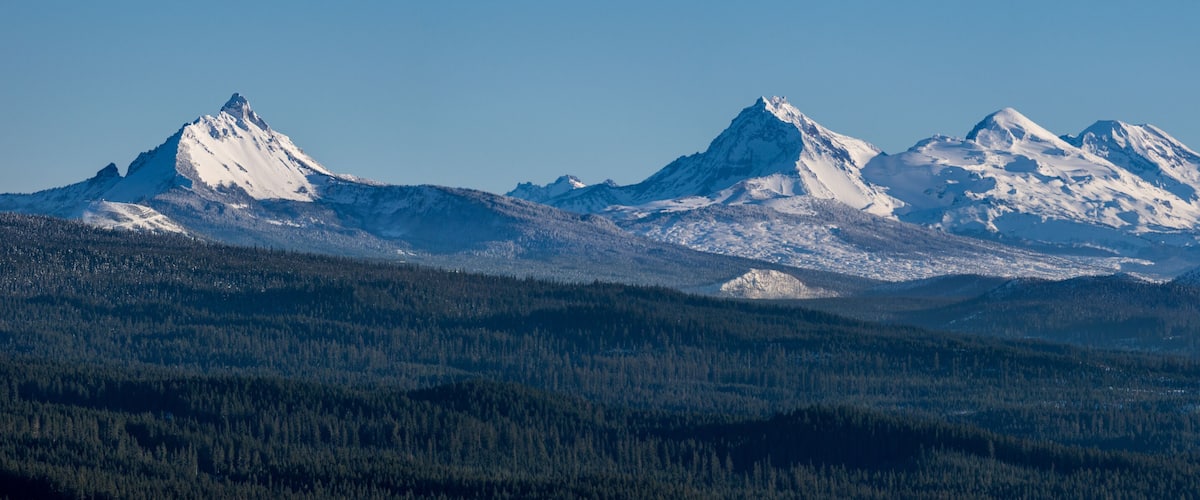 A snow-covered mountain range with dense forests at its base.