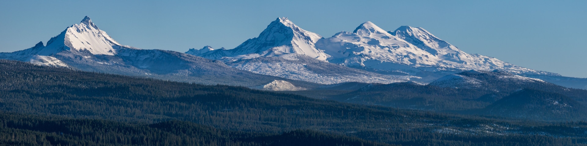 A snow-covered mountain range with dense forests at its base.