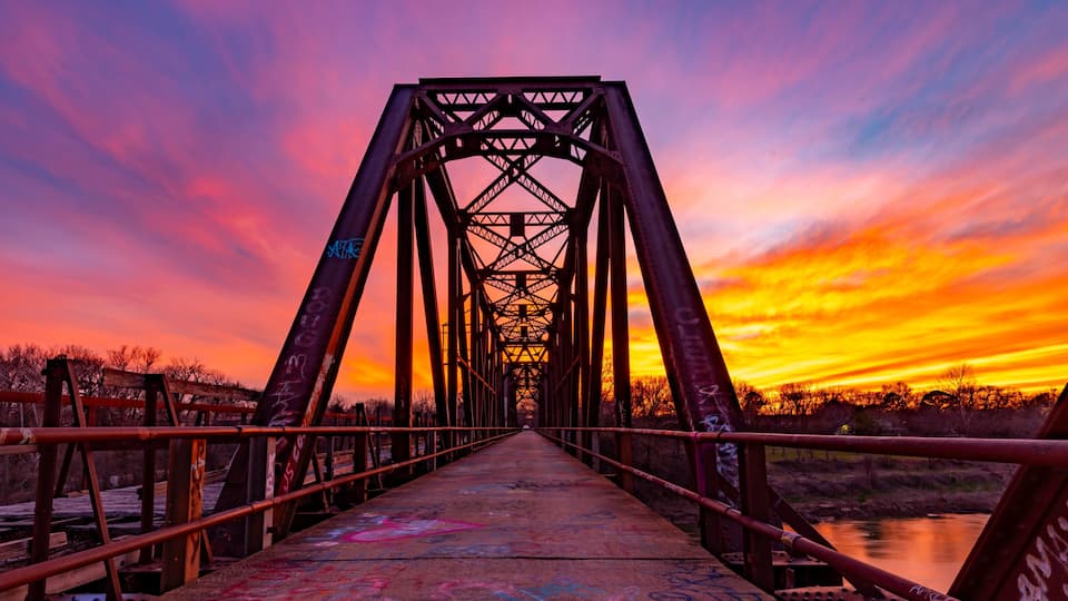 A sunset over a bridge with graffiti on the walkway.