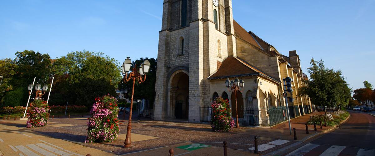 A historic church with a tall bell tower and a clock, surrounded by flower-lined streets and trees.