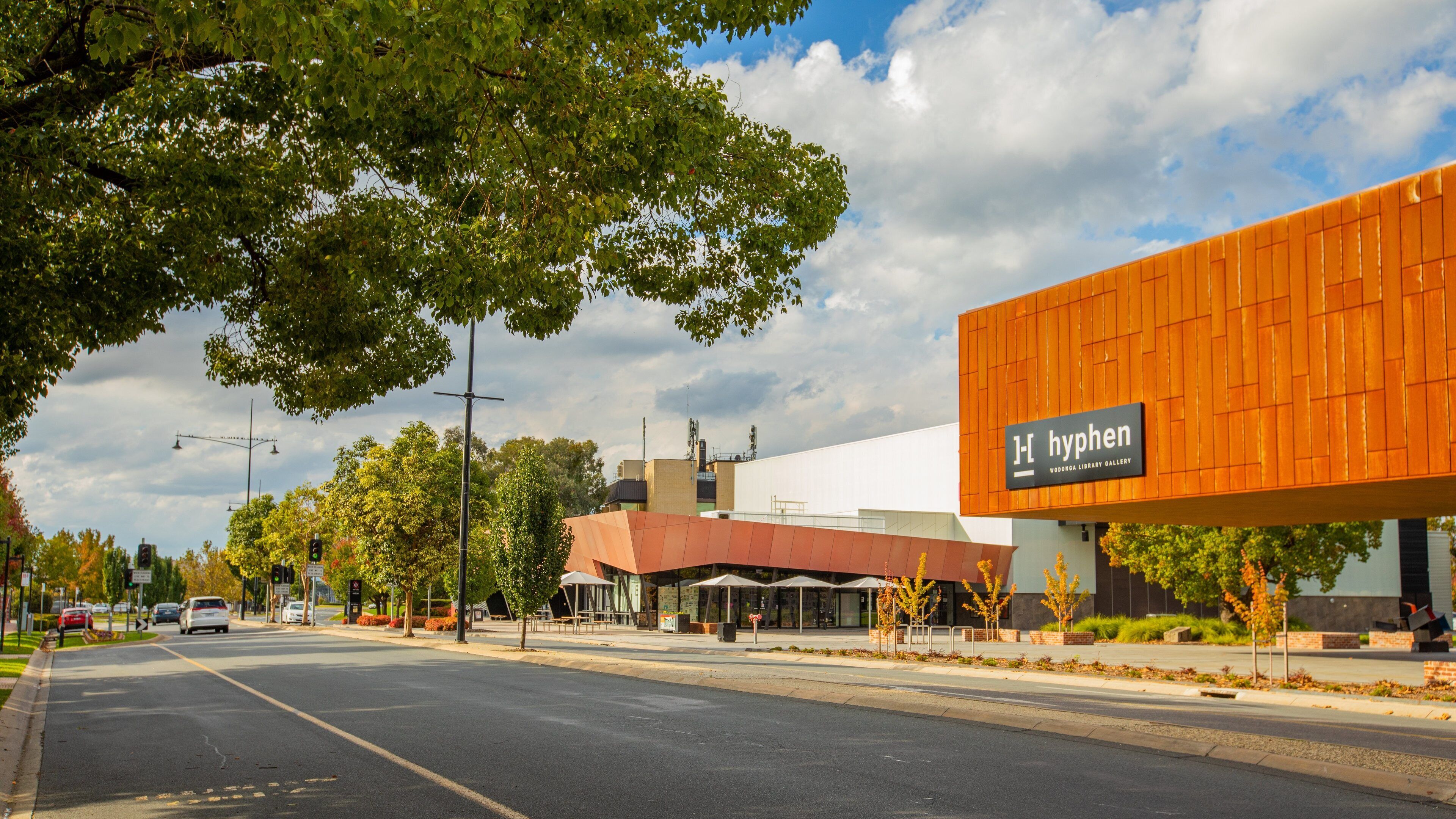 Un edificio moderno con un letrero que dice "hyphen" y una calle con coches y árboles.