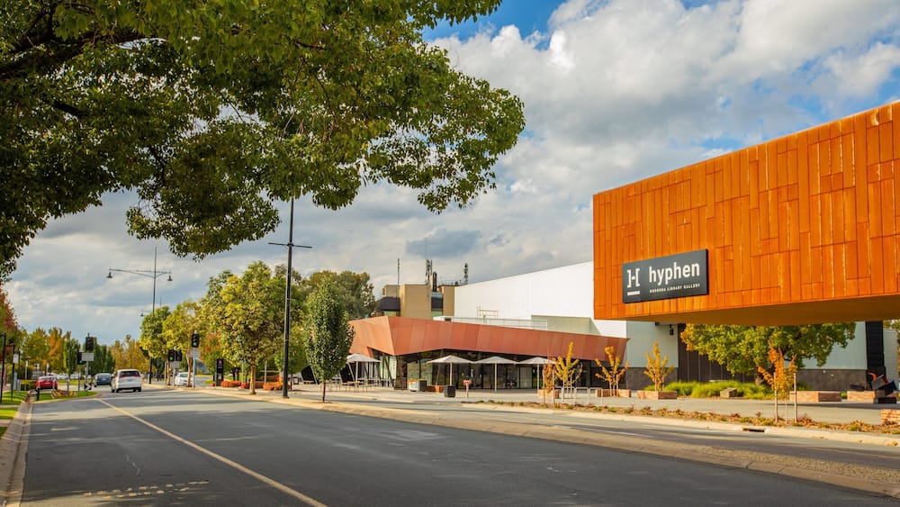 A modern building with a sign reading "hyphen" and a street with cars and trees.