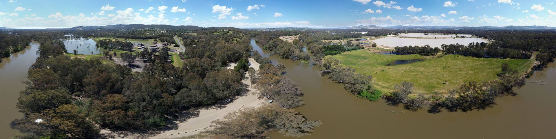 A river winding through a forested area with a large open field and a circular structure.