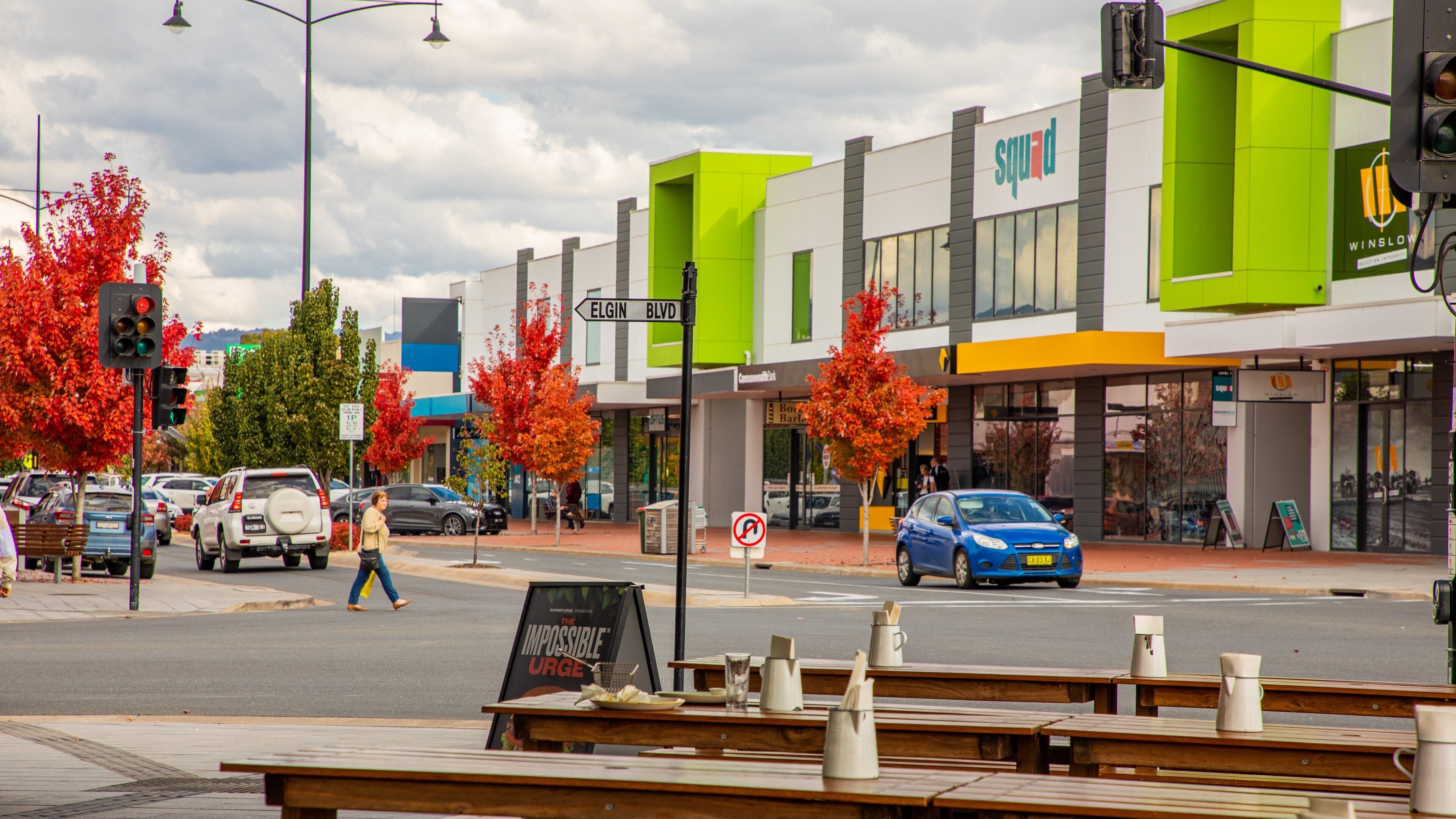 A street with a green building, a blue car, and a pedestrian crossing.