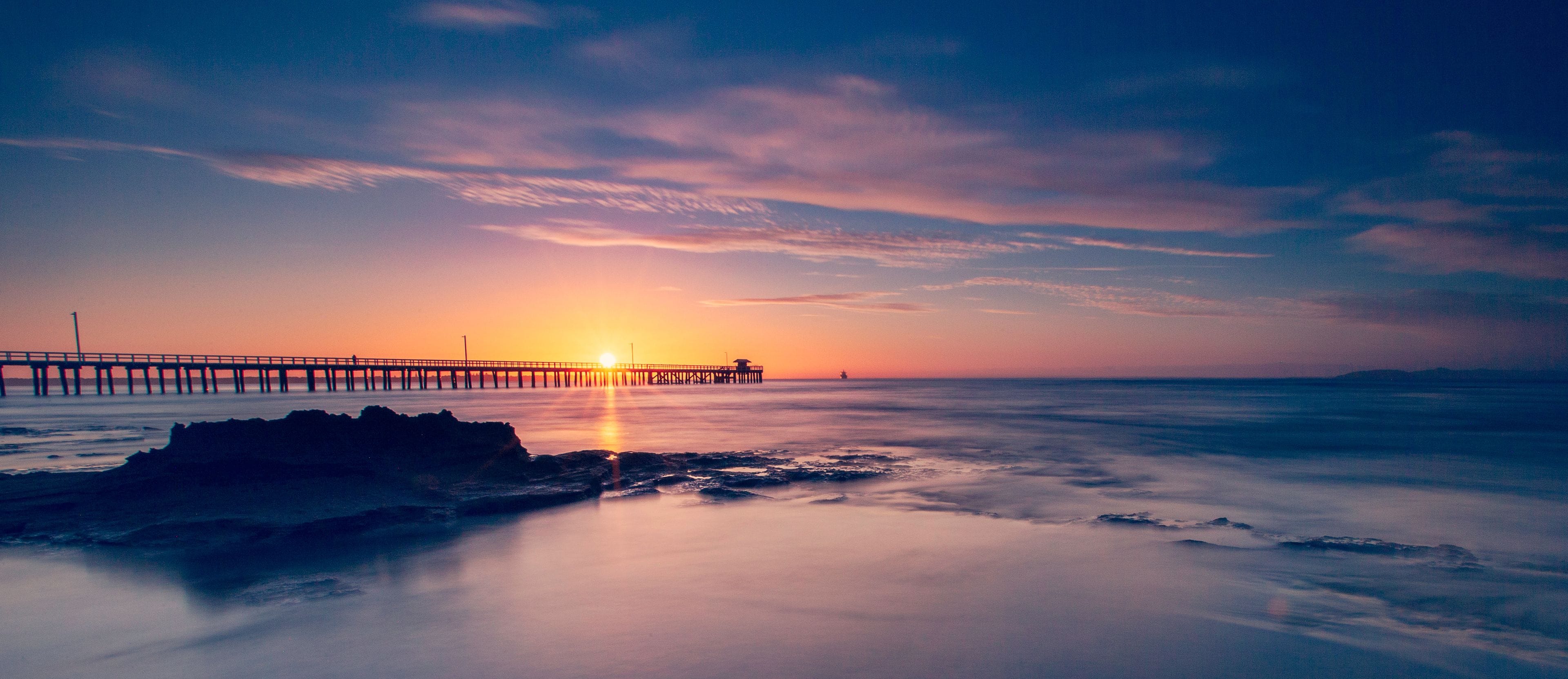 A sunset over a calm sea with a pier extending into the water.