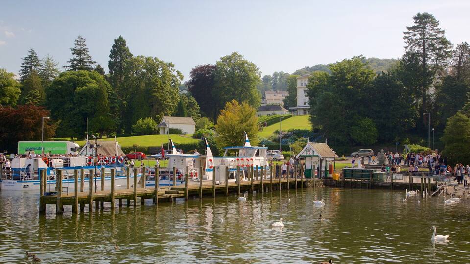 A riverside pier with boats, swans, and a crowd of people.