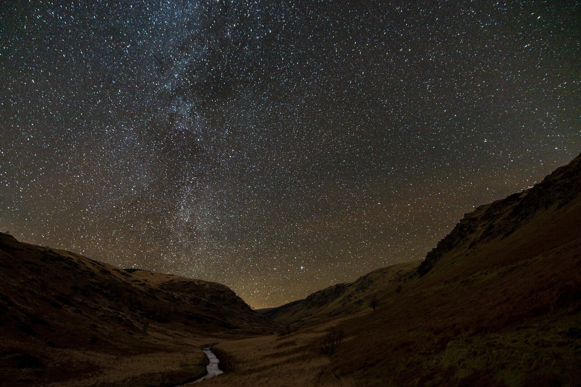 A starry night sky over a valley with a river.