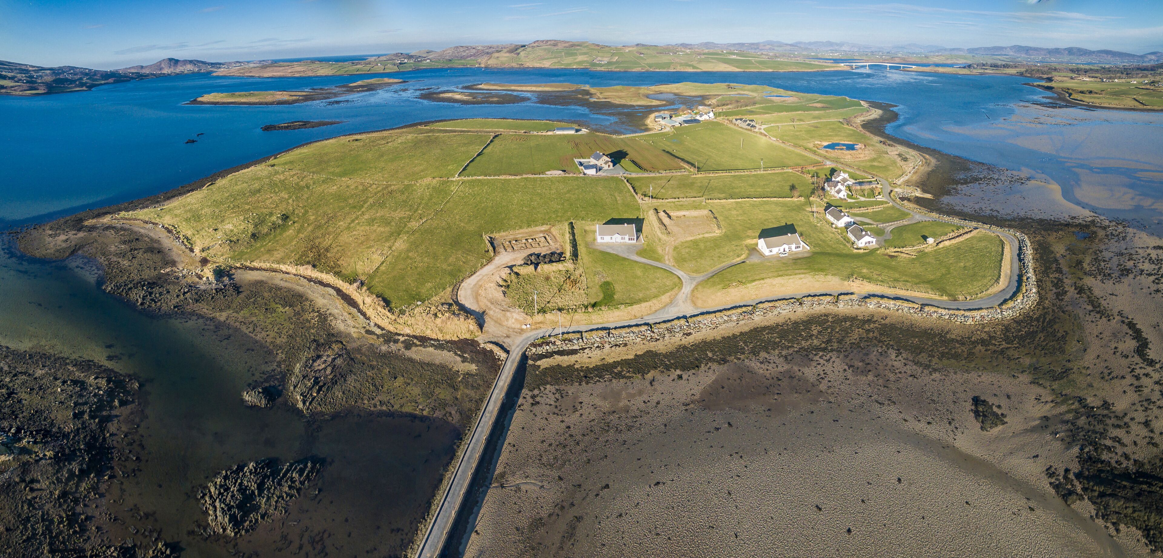 An aerial view of a coastal area with a mix of residential buildings, a road, and a bridge.