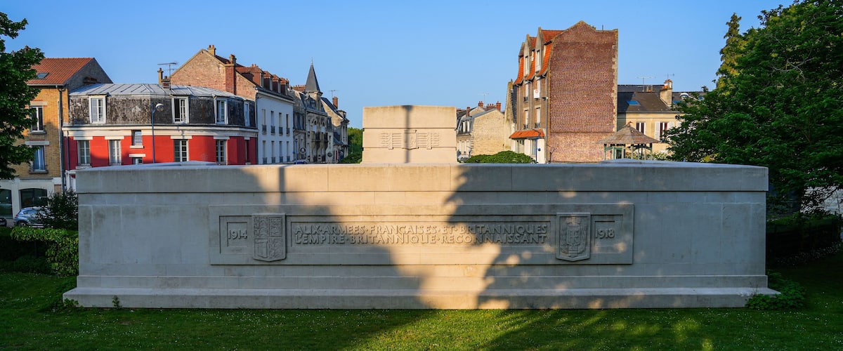 A stone monument with inscriptions and a plaque, surrounded by historic buildings and greenery.