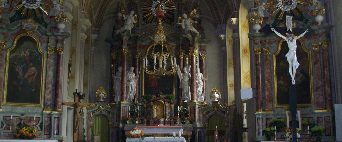An ornate church interior with a crucifix, statues, and a chandelier.
