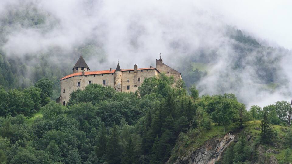 A castle surrounded by dense forest and mist.