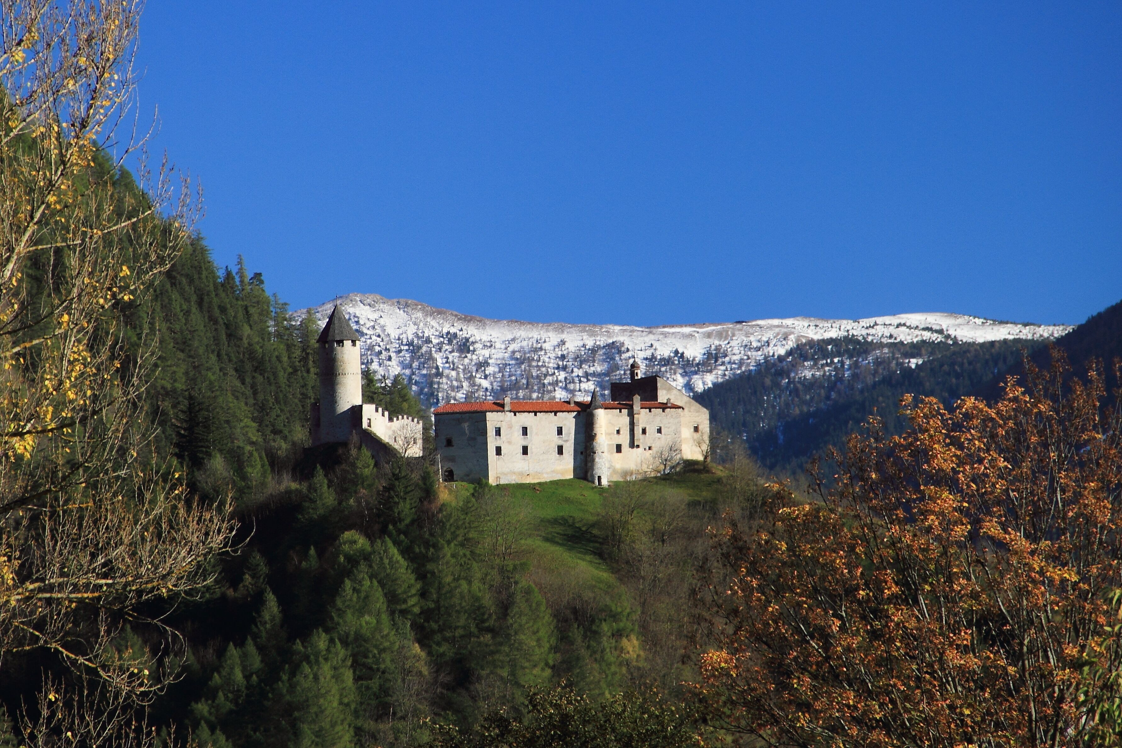 A castle on a hill with snow-capped mountains in the background.