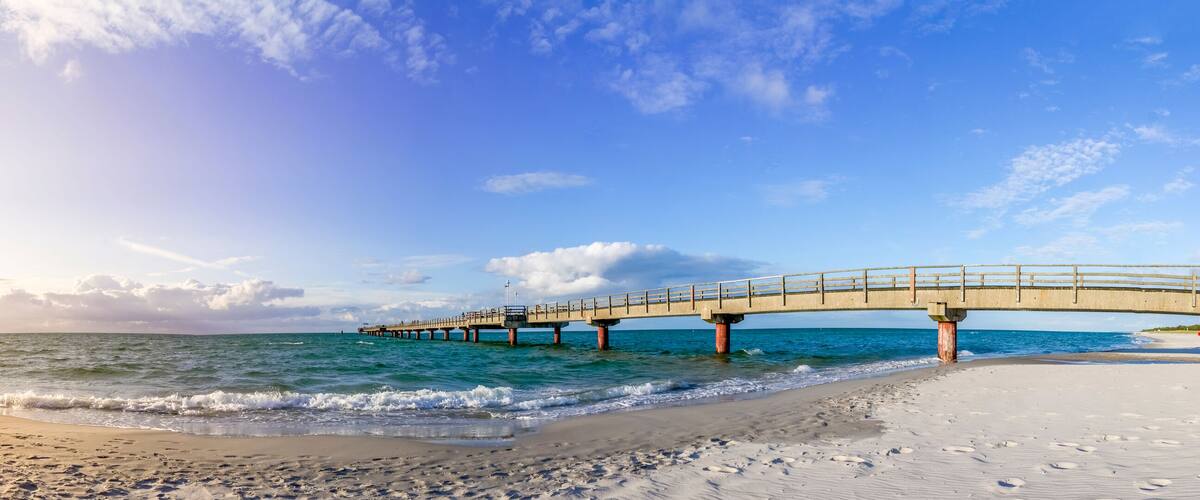 A beach with a wooden pier extending into the ocean, footprints in the sand, and a clear sky.
