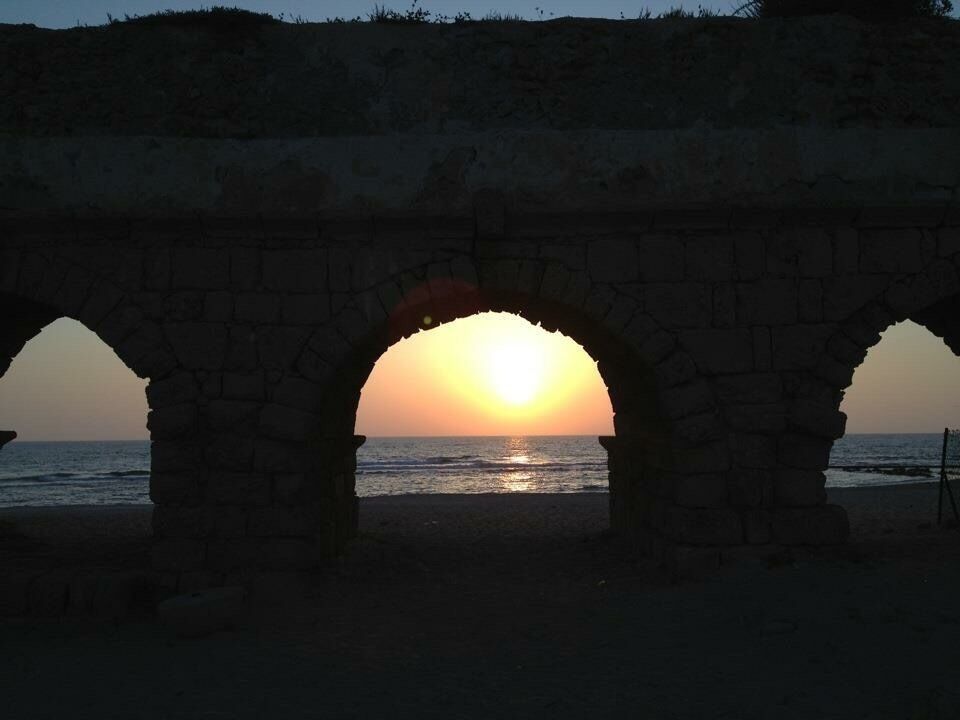 Un atardecer a través de arcos de piedra con vistas al mar.