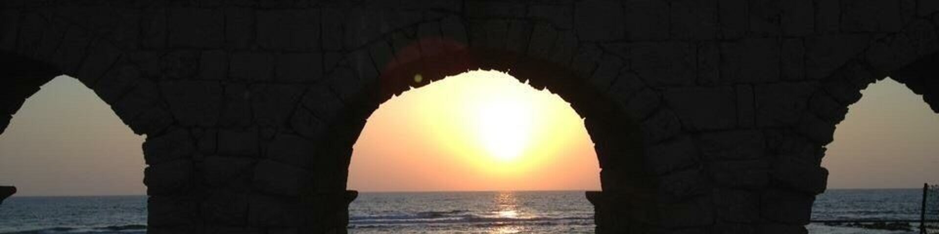 Un atardecer a través de arcos de piedra con vistas al mar.