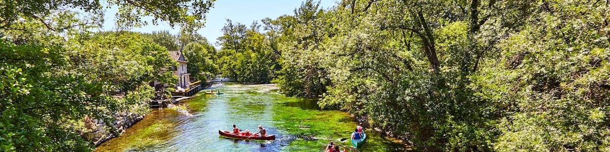 A river with kayaks, surrounded by dense greenery and a clear blue sky.