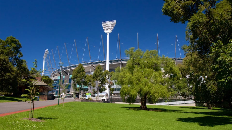 A stadium with a tall light tower, surrounded by trees and grass.