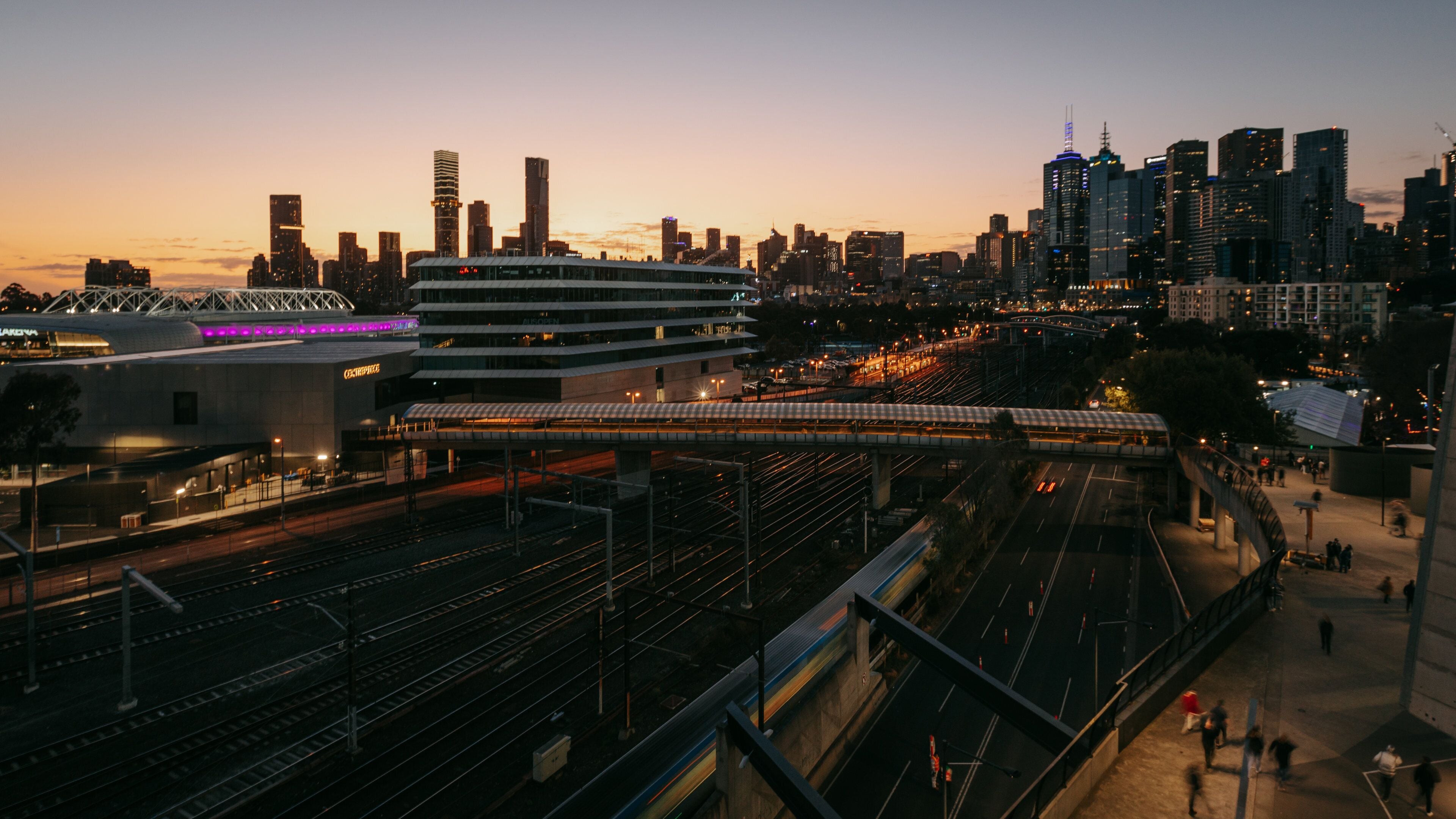 Un paisaje urbano al anochecer con una estación de tren moderna y vías de tren elevadas.