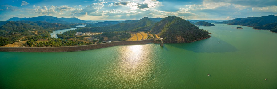 Uma grande extensão de água rodeada por colinas e uma pequena ilha com uma barragem.