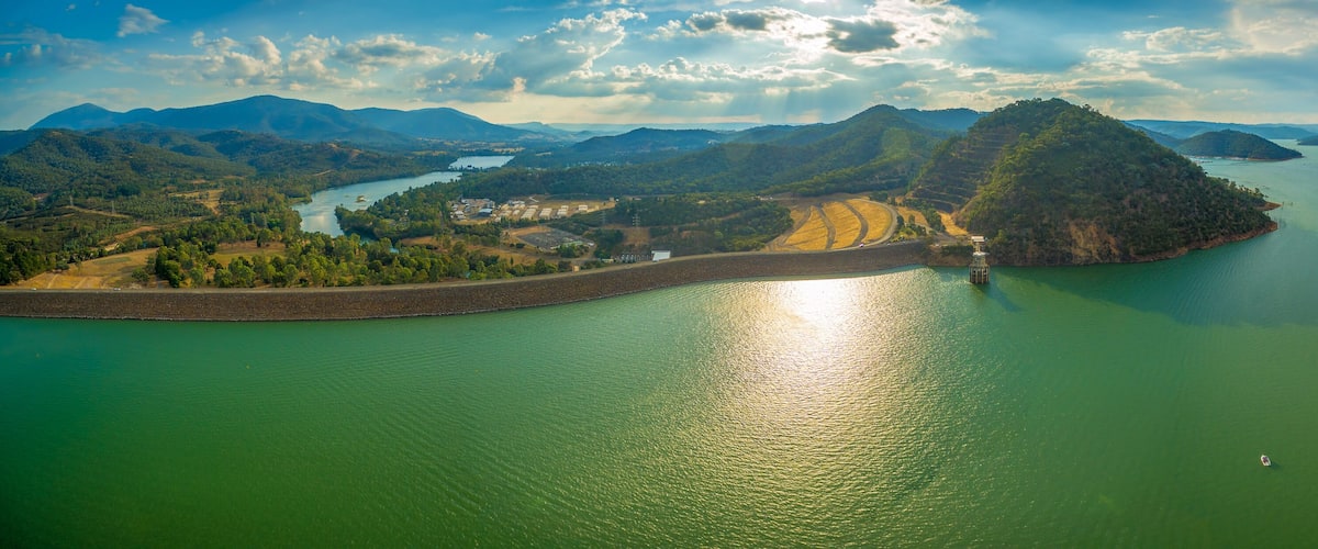A large body of water surrounded by hills and a small island with a dam.