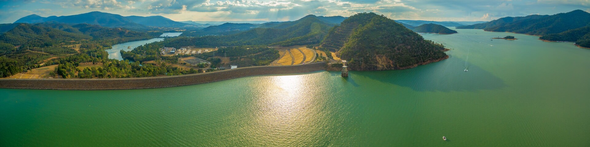 A large body of water surrounded by hills and a small island with a dam.