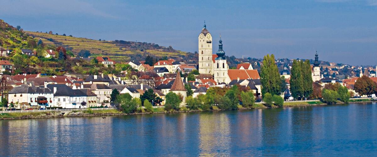 A river with a town, a prominent tower, and a hill in the background.