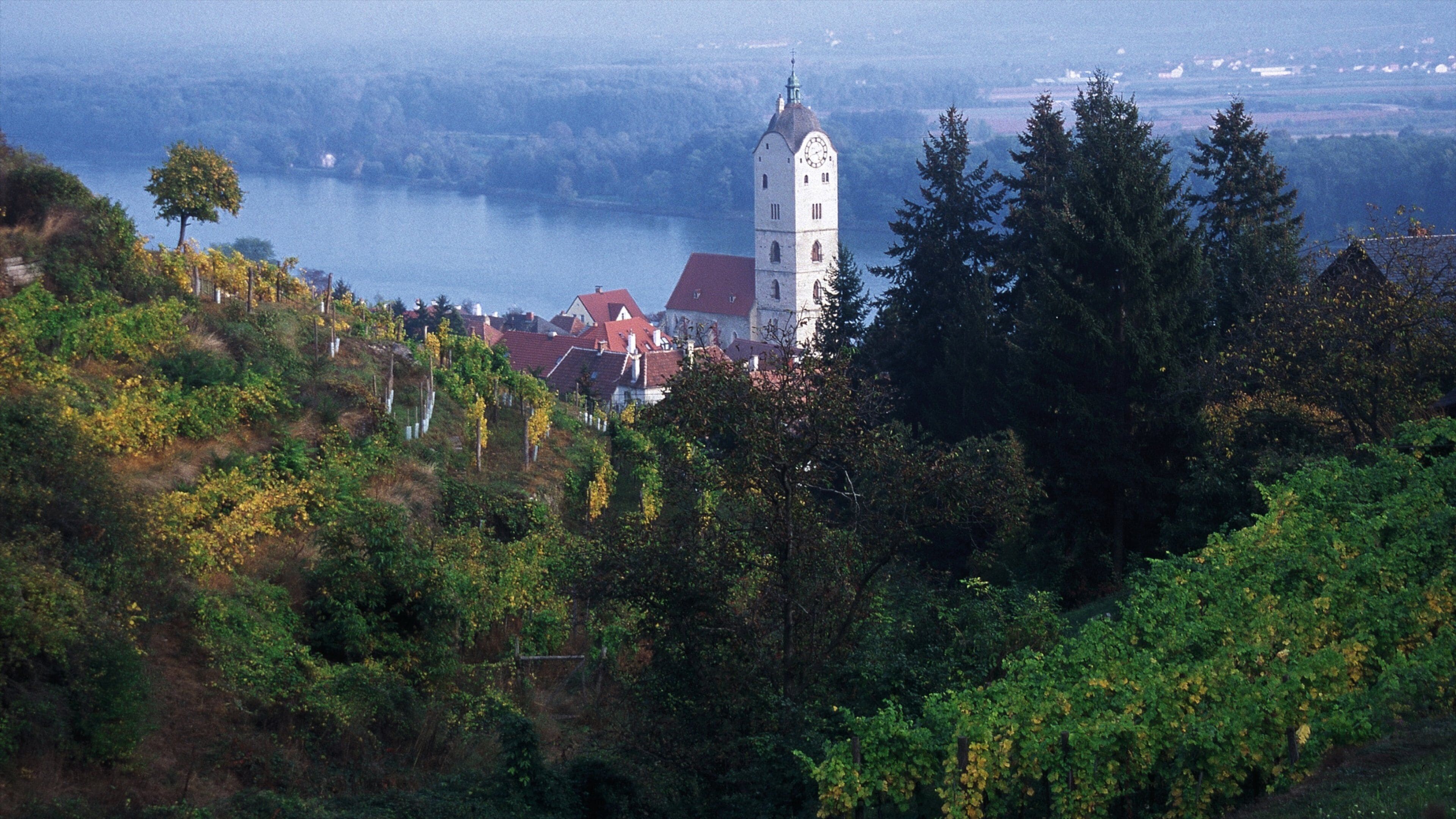 A tower with a clock, surrounded by trees and a lake.