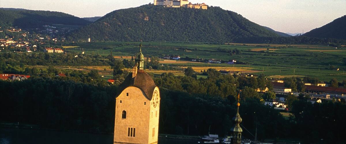 A tower with a clock, a river, and a castle on a hill.