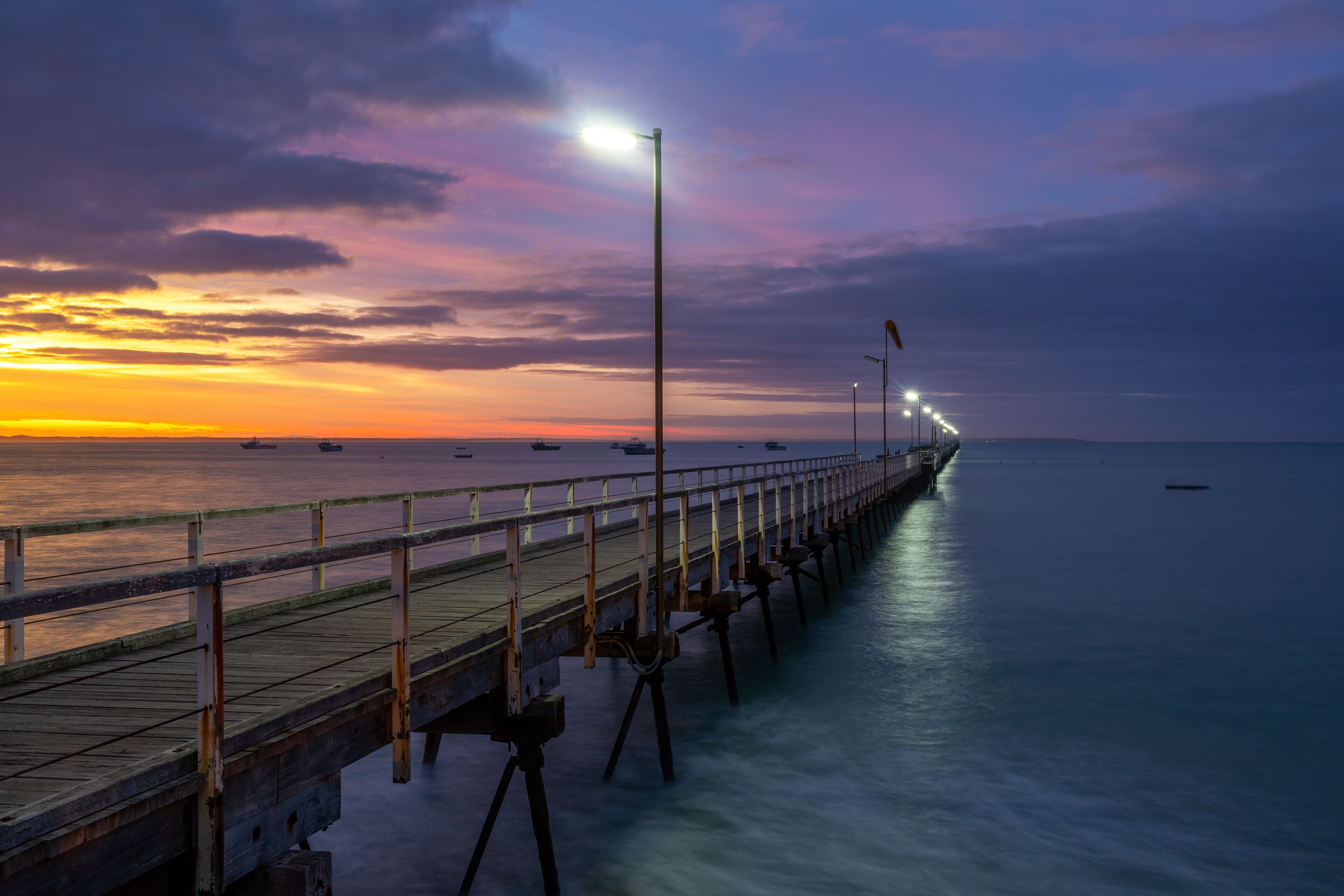 Un muelle se adentra en aguas tranquilas al atardecer, con un cielo lleno de colores.