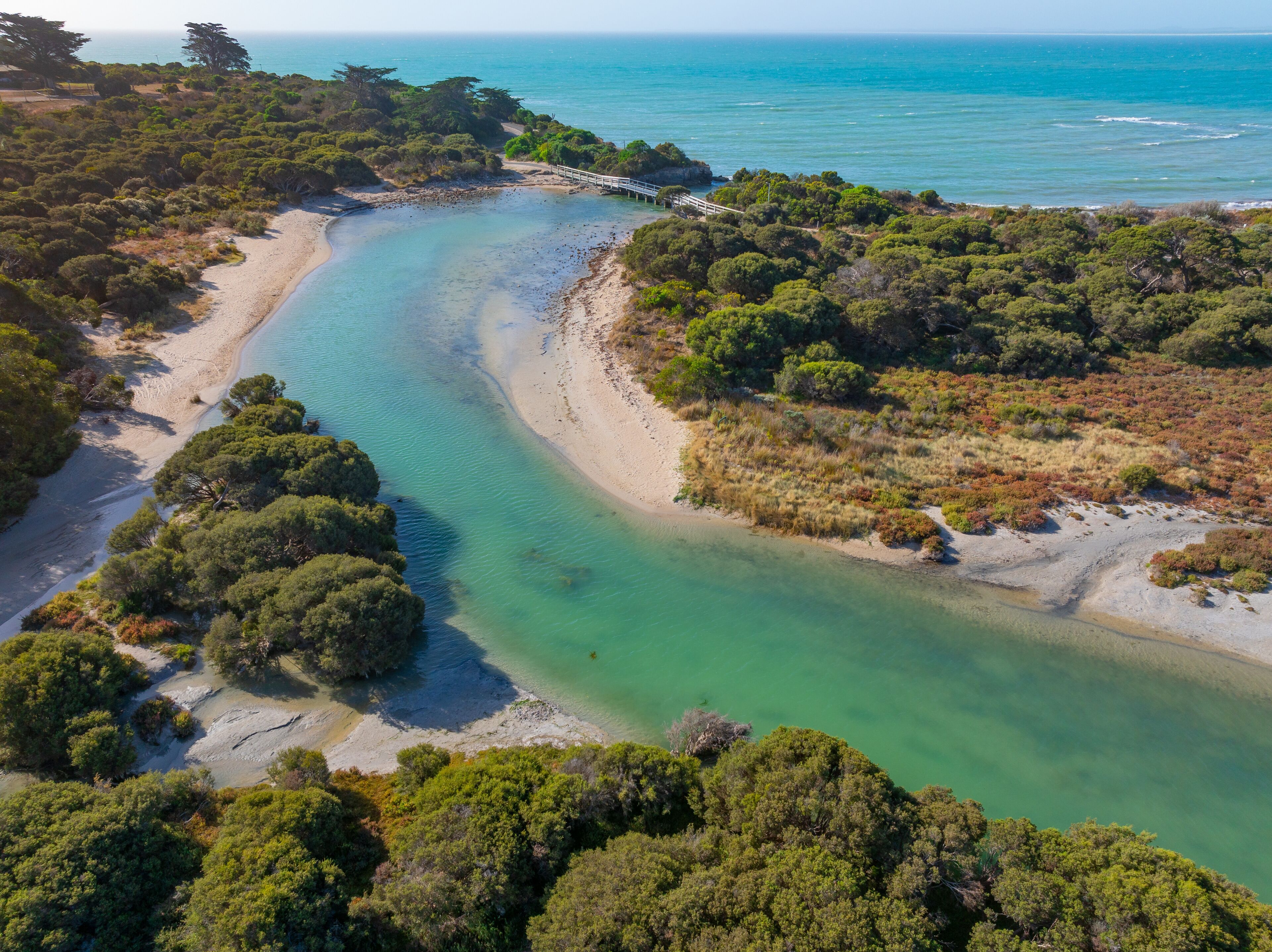 A coastal landscape with a clear turquoise river, sandy beach, and dense greenery.