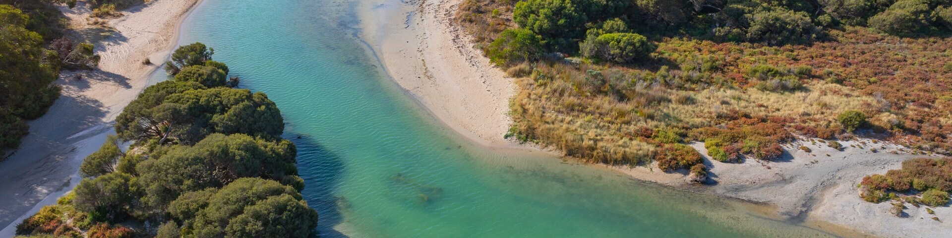 A coastal landscape with a clear turquoise river, sandy beach, and dense greenery.