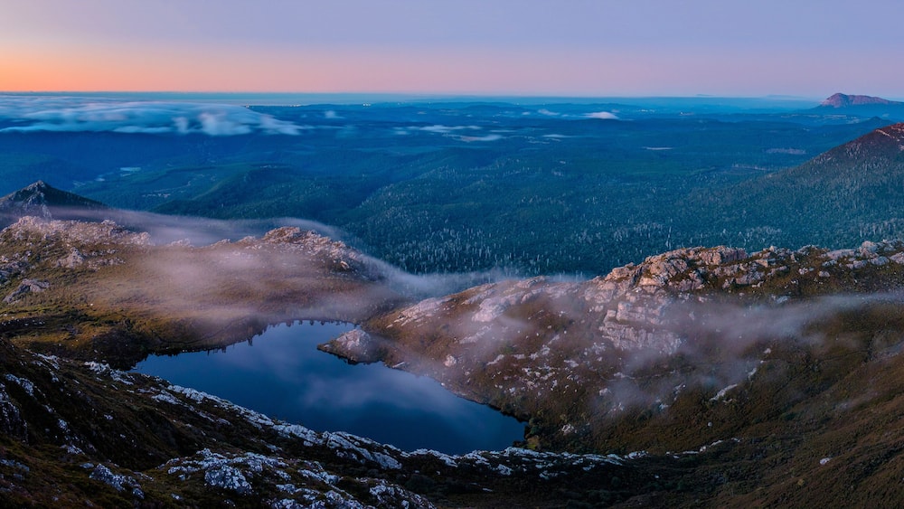 Un paysage montagneux avec un lac entouré de terrains rocheux et de zones boisées.