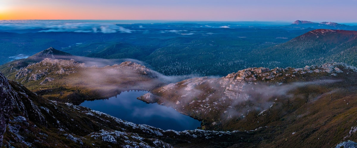 Eine gebirgige Landschaft mit einem See, umgeben von felsigem Gelände und bewaldeten Gebieten.